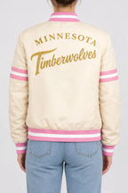 Women’s cream satin full-snap varsity jacket with gold script lettering across the back and pink striped rib trim
